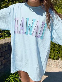 "Such a cute tee for summer! Comfort Colors chambray (light blue) t-shirt with \"HAWAII\" in blue and purple, with a black outline. Model is 5'4\" and wearing a size XL for an oversized look. 100% cotton." Light Blue Short Sleeve T-shirt For Summer, Trendy Light Blue Spring T-shirt, Casual Light Blue T-shirt For Summer, Light Blue T-shirt With Letter Print For Spring, Casual Light Blue Summer T-shirt, Light Blue Crew Neck T-shirt With Text Print, Casual Purple Beach T-shirt, Casual Purple T-shirt For Beach, Purple Graphic Print Tops For Vacation