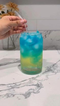 a hand holding a straw in a blue and green drink on a marble counter top