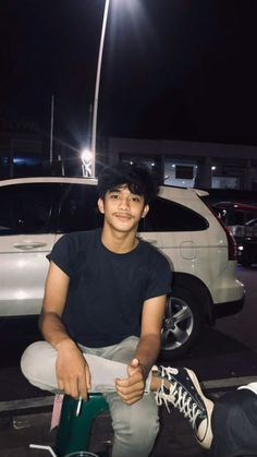 a young man sitting on top of a green chair next to a white car at night