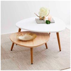 a white coffee table with wooden legs and a flower vase on the top, in front of a beige rug