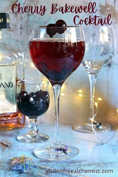 two glasses filled with red wine and cherries on a table next to bottles of alcohol