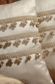 two white pillows with beaded trim and pearls on the sides are sitting next to each other