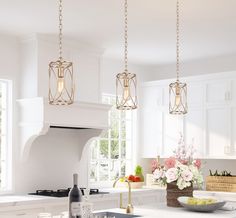 a kitchen with white cabinets and an island in front of the stove top, has three pendant lights hanging from the ceiling