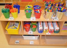 a wooden shelf filled with lots of different colored pens and pencils in buckets