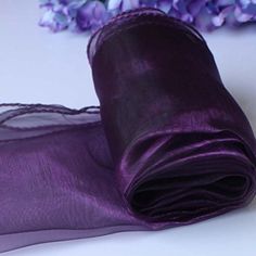 purple satin fabric with lace edge on white tablecloths and flowers in the background