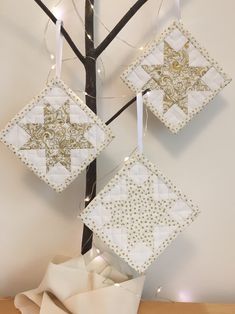 three white and gold ornaments hanging from a tree branch in front of a wall with lights