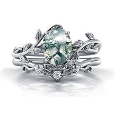 a white gold ring with an oval green stone surrounded by leaves and diamonds on the sides