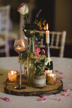 a table topped with candles and vases filled with flowers next to bottles of wine