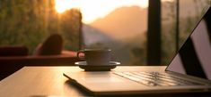 a laptop computer sitting on top of a wooden table next to a cup of coffee