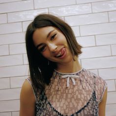 a woman standing in front of a white brick wall with her tongue out and looking at the camera