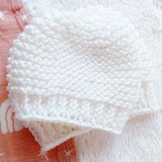 a white knitted blanket laying on top of a bed next to a pink pillow