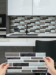 two hands are holding tiles in front of a kitchen counter