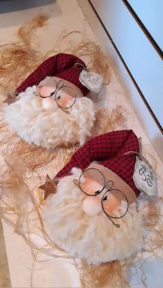 two stuffed santa clauss are sitting on the counter top, one is wearing glasses and the other has long hair