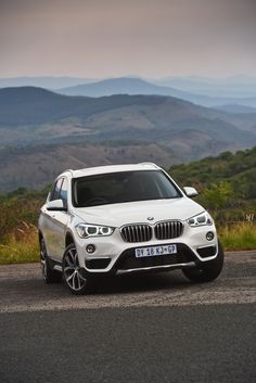 a white bmw suv parked on the side of a road with mountains in the background