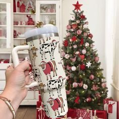 a person holding a coffee cup in front of a christmas tree with cows on it