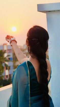 a woman in a green sari is holding her hand up to the sun set