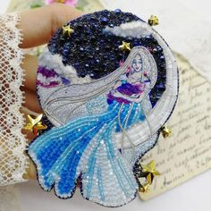 there is a hand holding a brooch with an image of a mermaid on it