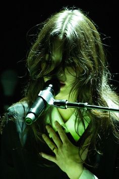 a woman with long hair holding a microphone in front of her face and looking down