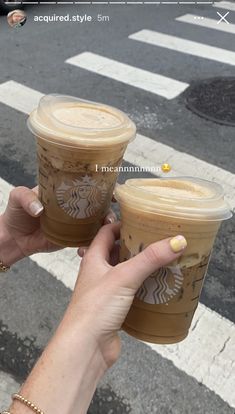 two cups of coffee are being held up by someone's hands on the street