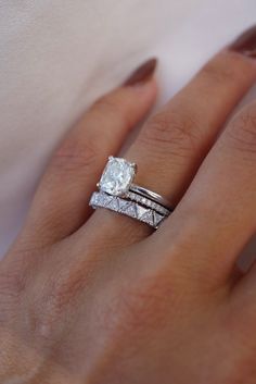 a woman's hand with two wedding rings on top of her finger and the ring has a diamond in it