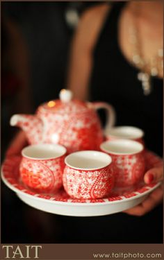 a red and white tea set on a plate with four cups in front of it