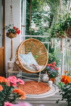 a hanging chair on a porch with flowers and potted plants