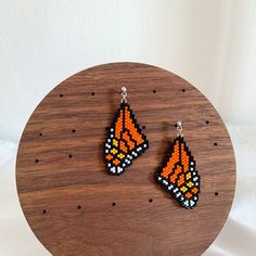 two orange and black beaded earrings sitting on top of a wooden table next to a white wall