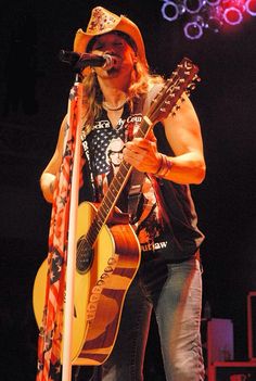 a man with a cowboy hat and guitar sings into a microphone while holding an american flag