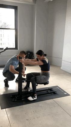 a man and woman doing squats on exercise mats in an office space with windows