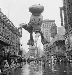 an inflatable mickey mouse balloon floats through the air on a wet city street