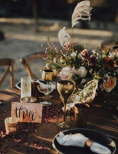 there is a table set with wine glasses and flowers on it, along with place cards