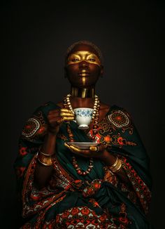 an african woman holding a cup and saucer in her hands with gold paint on her face