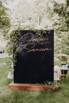 a black sign with gold writing on it sitting in the middle of a grass covered field