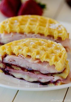 two ham and cheese waffle sandwiches on a white plate with strawberries in the background