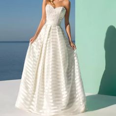 a woman in a white wedding dress standing by the ocean with her hands on her hips