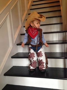 a little boy wearing a cowboy hat and bandana standing on some stairs with his hands in his pockets