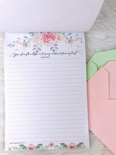 an open notepad with flowers on it next to a pink envelope and green envelope