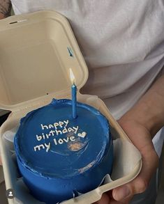 a man holding a blue birthday cake with a candle in it