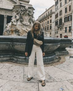 a woman standing in front of a fountain with her hands on her hips and looking at the camera