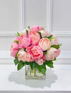 a vase filled with pink flowers sitting on top of a white table next to a wall