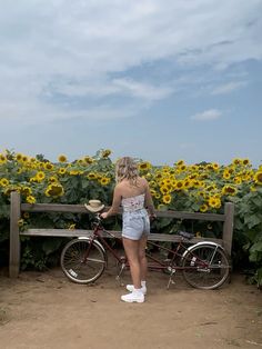 a woman standing next to a bike in front of a field of sunflowers