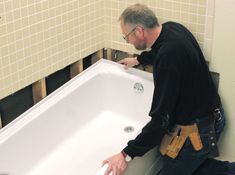 a man in black shirt and jeans fixing a bathtub