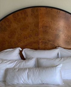 a large wooden headboard with white pillows on the top and bottom, in front of a beige wall