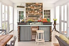 an outdoor kitchen with stone wall and bar stools in the center, surrounded by large windows