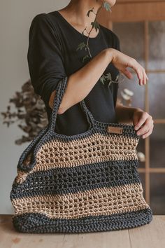 a woman holding a crocheted bag on top of a wooden table next to a potted plant