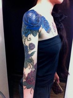 a woman with a blue rose tattoo on her arm and shoulder is standing in front of a mirror