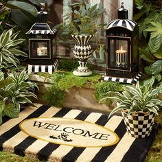 a welcome mat is on the ground in front of some plants and potted plants