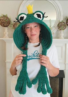 a woman wearing a green frog hat and scarf in front of a fireplace with her hands on her hips