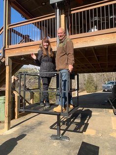 a man and woman standing next to each other in front of a wooden structure with stairs