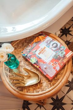 a magazine and flowers on a wooden table next to a white bath tub in a bathroom